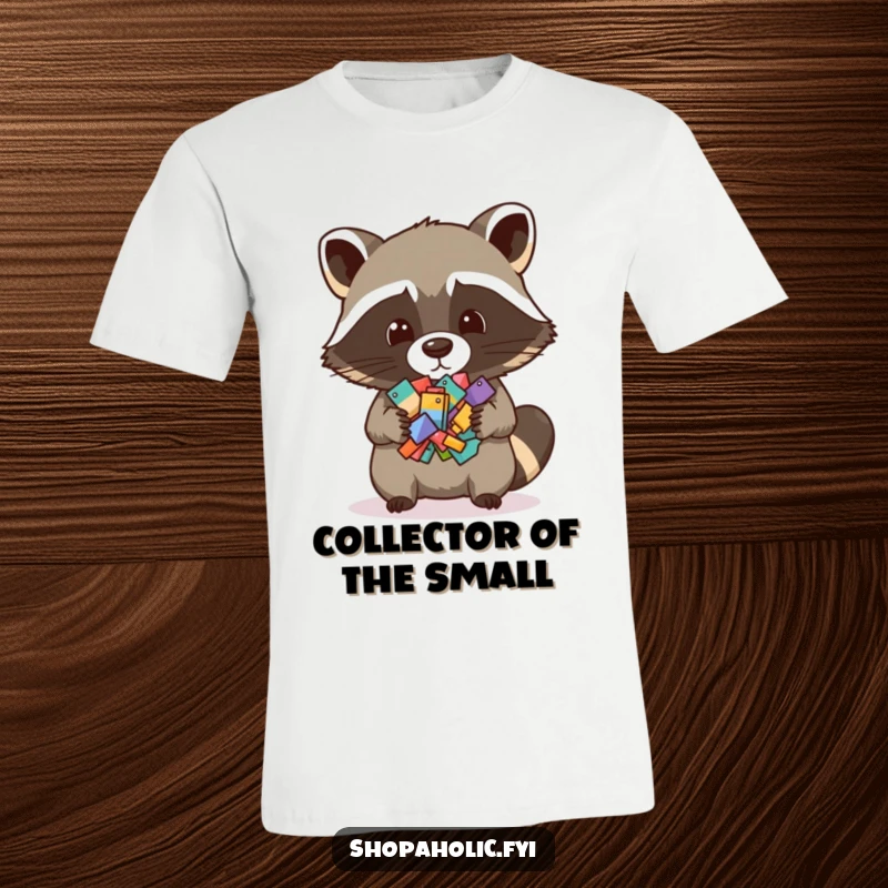 Funny t-shirt featuring a mischievous raccoon holding a large pile of various small items, highlighting collecting and hoarding humor.